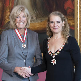 The Governor General shakes the hand of Sally Wishart Armstrong.  Both are wearing their Order of Canada insignia. 