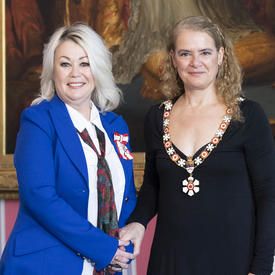 The Governor General shakes the hand of Jann Arden Richards.  Both are wearing their Order of Canada insignia. 
