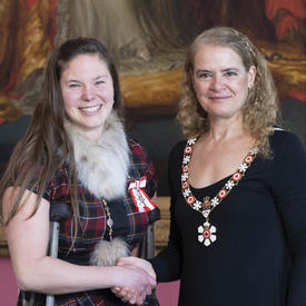 The Governor General shakes the hand of Stephanie Dixon.  Both are wearing their Order of Canada insignia. 