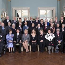 A group photo of the 35 people invested into the Order of Canada with Governor General Julie Payette. They are arranged in three rows, the first sitting and the others standing. 