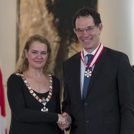 Neil G. Turok  se tient à côté de la Gouverneure générale.  Tous deux sourient à la caméra.  Ils portent leur insigne de l'Ordre du Canada.