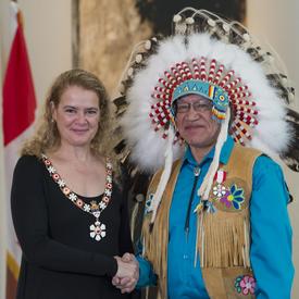 Edmund Metatawabin stands next to the Governor General.  Both smile at the camera.  They are wearing their Order of Canada insignia.