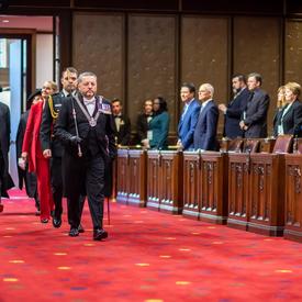 The Governor General, led by the Usher of the Black Rod, enters the Senate Chamber. 