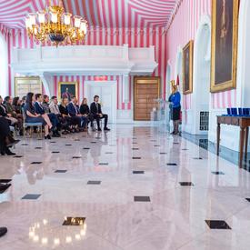 Side view of Ms. Assunta Di Lorenzo speaking at a podium in front of an audience in Rideau Hall's red, black and white tent room.
