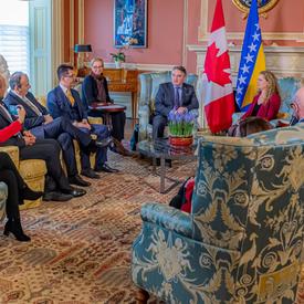  Canadian government officials and members of the Bosnia and Herzegovina delegation attend a meeting with the Governor General and His Excellency Željko Komšić. Everyone is sitting in chairs. 
