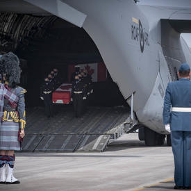 CAF members, including a bagpiper watch as a coffin, carried by CAF members, is taken off a plane.
