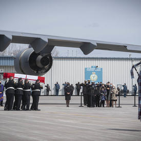 Les membres des FAC transportent un cercueil jusqu'au corbillard. Un cornemuseur est au premier plan. 