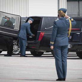 The Governor General salutes a coffin as it is placed in a hearse. 