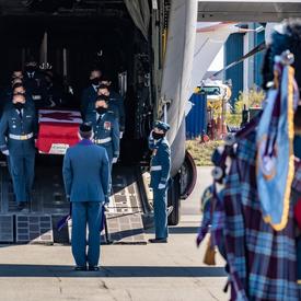 Captain Jennifer Casey’s coffin is carried off the plane by Canadian Armed Forces members. A bag pipe player is in the foreground of the picture. 