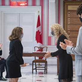 A woman is standing facing Governor General Payette and Prime Minister Trudeau who are applauding.