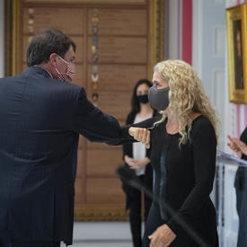 Un homme et une femme se touchent les coudes pour remplacer une poignée de main tandis qu'un petit public applaudit. Tous les participants portent un masque facial.