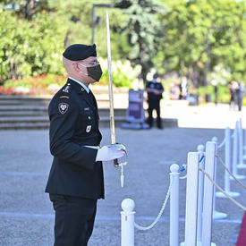 A military member in service dress holds a sword in front of him. A woman dressed in white is standing in front of him. 