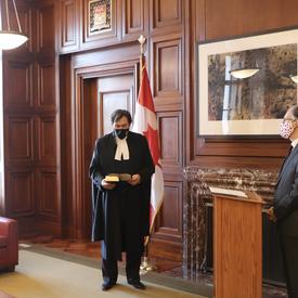 Chief Justice Richard Wagner holding a book. Ian Shugart - clerk of the Privy Council of Canada - stands a podium. 