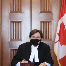 Chief Justice Richard Wagner sitting at a table, signing a document. He is looking at the camera.