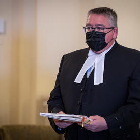 Un homme, portant une tenue noire avec un col blanc, tient des documents.