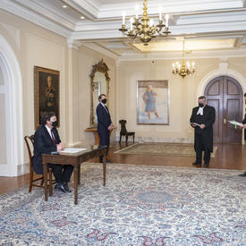 Three people standing at a distance while the Administrator, seated at a table, signs a document.