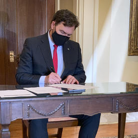 The Administrator sitting at a table, signing a document.