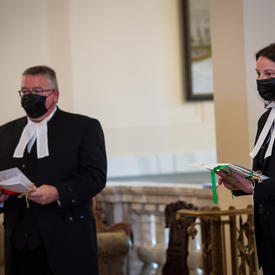 Two people, both dressed in black with white collars, each holding documents.