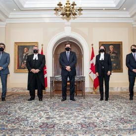 The Administrator flanked on either side by two people. All wearing masks. Two Canadian flags in the background. 