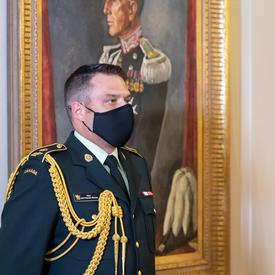 An aide-de-camp standing next to a portrait.