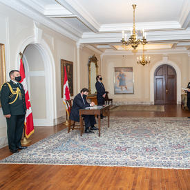 Four people standing at a distance while the Administrator, seated at a table, signs a document.