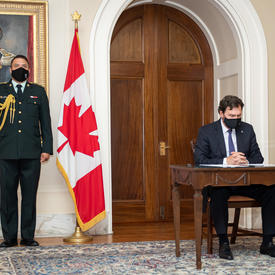 The Administrator sitting at a table. An aide-de-camp is standing to his right.