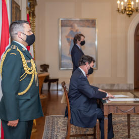 An aide-de-camp standing as the Administrator sits at a table. The Secretary is visible in the background.