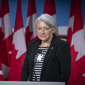 Governor General Designate Mary May Simon stands at a podium in front of several Canadian flags.