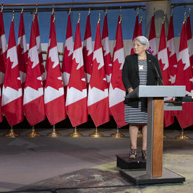 Prime Minister Justin Trudeau and Governor General Designate Mary May Simon each stand at a podium with several Canadian flags behind them.