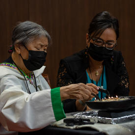 An Inuit Elder lighting the qulliq in the Senate. A woman is seated beside her. 