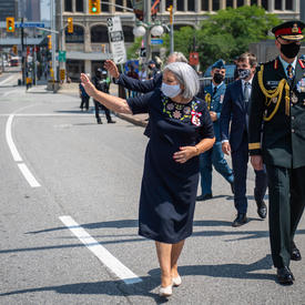 Governor General Mary May Simon waving to the crowd as she walks from the Senate to the National War Memorial.
