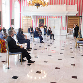 View of the Tent Room at Rideau Hall. Striped walls and marble floor with guests in chairs.