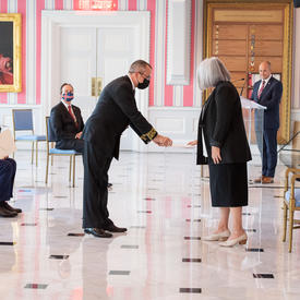 A man in a suit and a face mask hands a document to the Governor General.