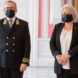 A man in a suit and a face mask stands to right of Governor General Mary May Simon as they pose for a photo.