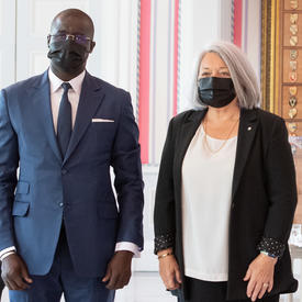A man in a suit and a face mask stands to right of Governor General Mary May Simon as they pose for a photo.