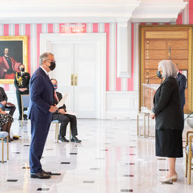 A man in a suit and a face mask hands a document to the Governor General.