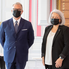 A man in a suit and a face mask stands to right of Governor General Mary May Simon as they pose for a photo.
