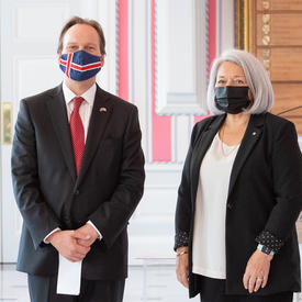 A man in a suit and a face mask stands to right of Governor General Mary May Simon as they pose for a photo.