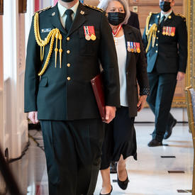 A procession of people, including the Governor General, makes its way into a room.