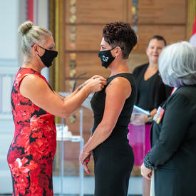 A woman in a brightly coloured dress pins a medal onto the black dress of another woman. 