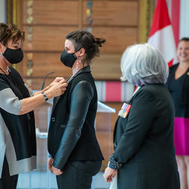 A woman pins a medal onto another woman’s dress jacket.