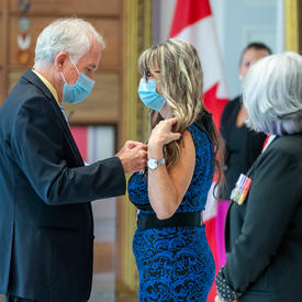 Un homme épingle une médaille sur la robe bleue et noire d’une femme.