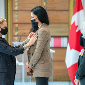 A woman pins a medal onto another woman’s dress jacket.
