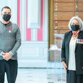 Un homme fraîchement décoré d’une médaille se tient près de la gouverneure générale Mary May Simon. Tous deux portent un masque.