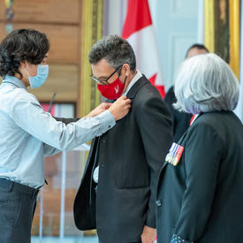 A young man pins a medal onto a man’s jacket.