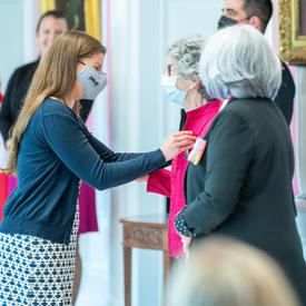 Une jeune femme épingle une médaille sur le blouson fuchsia d’une femme.
