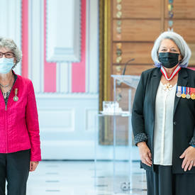 A woman who has just been given a medal stands next to Governor General Mary May Simon. Both are wearing masks.