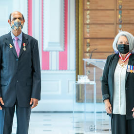 A man who has just been given a medal stands next to Governor General Mary May Simon. Both are wearing masks.