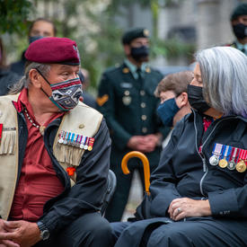 The Governor General speaks with a man seated to her right. Both wear masks.