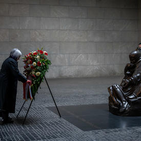 Governor General Mary May Simon is laying a large wreath.There are people standing along the wall behind her.